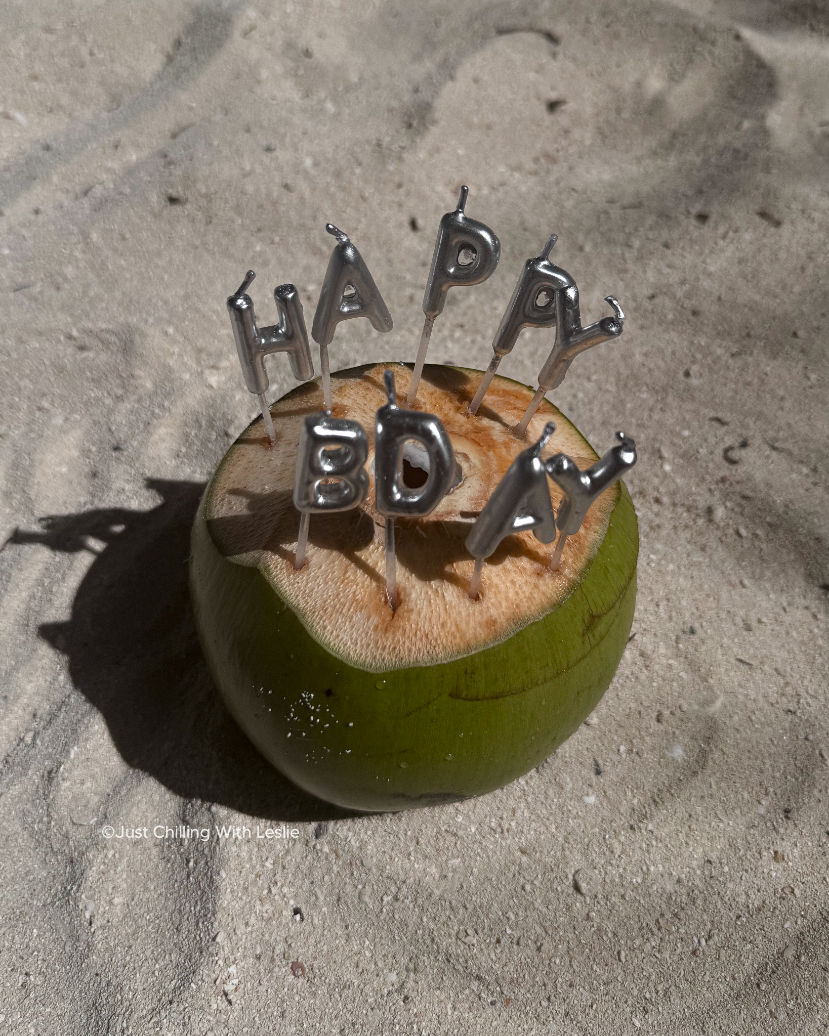 a coconut with birthday candles on a beach in aruba by Leslie Harris